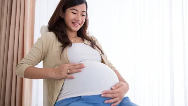 happy pregnant asian woman touching her big belly while sitting 720x405