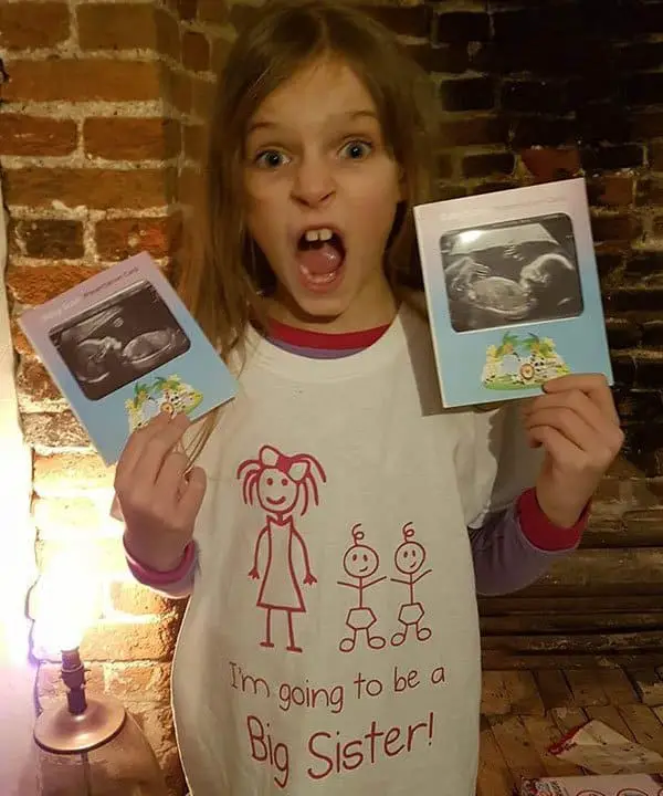 Big sister holding twin ultrasound scan pictures for twin pregnancy announcement